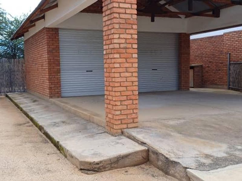 A double garage featuring exposed brick construction, roller shutter doors, and a covered concrete parking area.