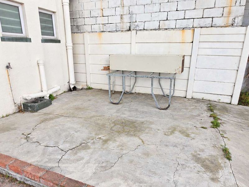 A rear exterior area featuring concrete paving, a boundary wall, and an external water tap, showing signs of wear and weathering.