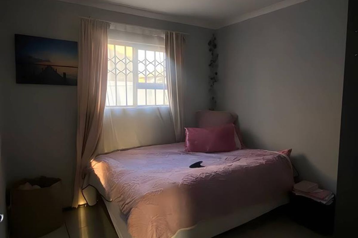 A bedroom featuring tiled flooring, a window with security bars, and a central ceiling light fixture.