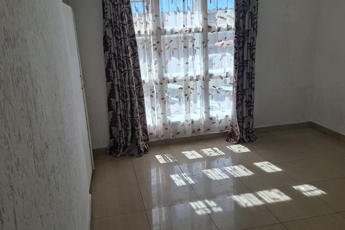 A bright, empty bedroom featuring tiled flooring and a large window with curtain tracks, offering a blank canvas for personalization.