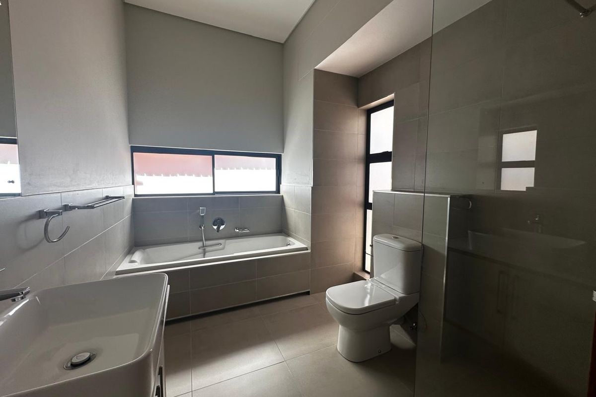 Modern bathroom featuring a built-in bathtub, a wall-mounted vanity basin, a toilet, and a glass-enclosed shower area with neutral floor-to-ceiling tiling.
