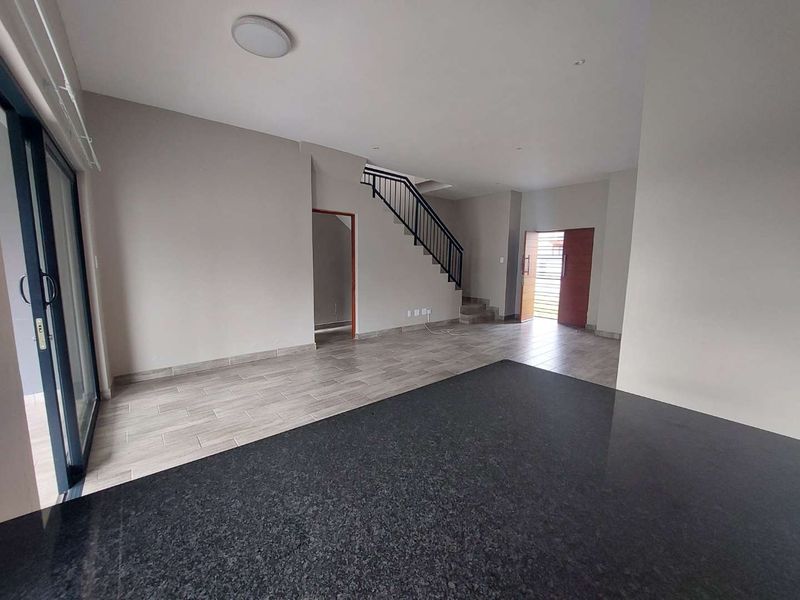 Spacious open-plan living area featuring tiled flooring, a large granite kitchen island, and a staircase with a modern metal railing.