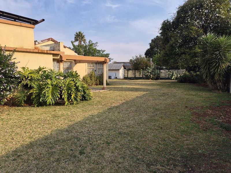 A spacious rear garden featuring a covered patio area with concrete columns, established landscaping, and a perimeter wall.