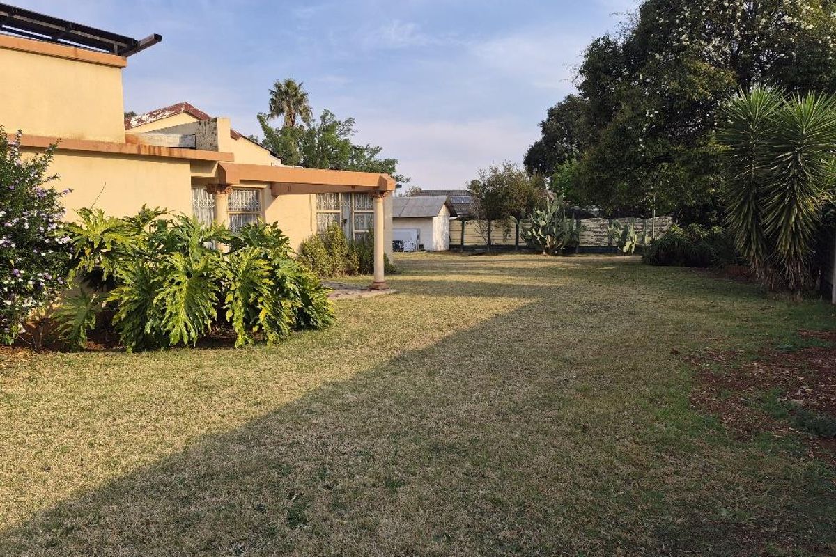 A spacious rear garden featuring a covered patio area with concrete columns, established landscaping, and a perimeter wall.