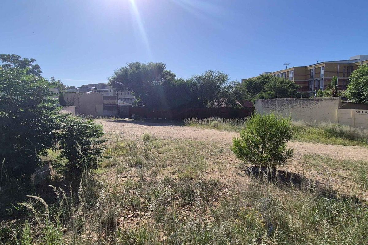 A vacant residential plot featuring natural vegetation, enclosed by a perimeter wall with integrated electric fencing.
