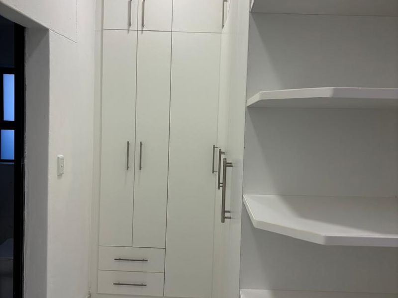 A clean, modern dressing area or bedroom space featuring white built-in cupboards, open shelving, and polished marble-look tiled flooring.
