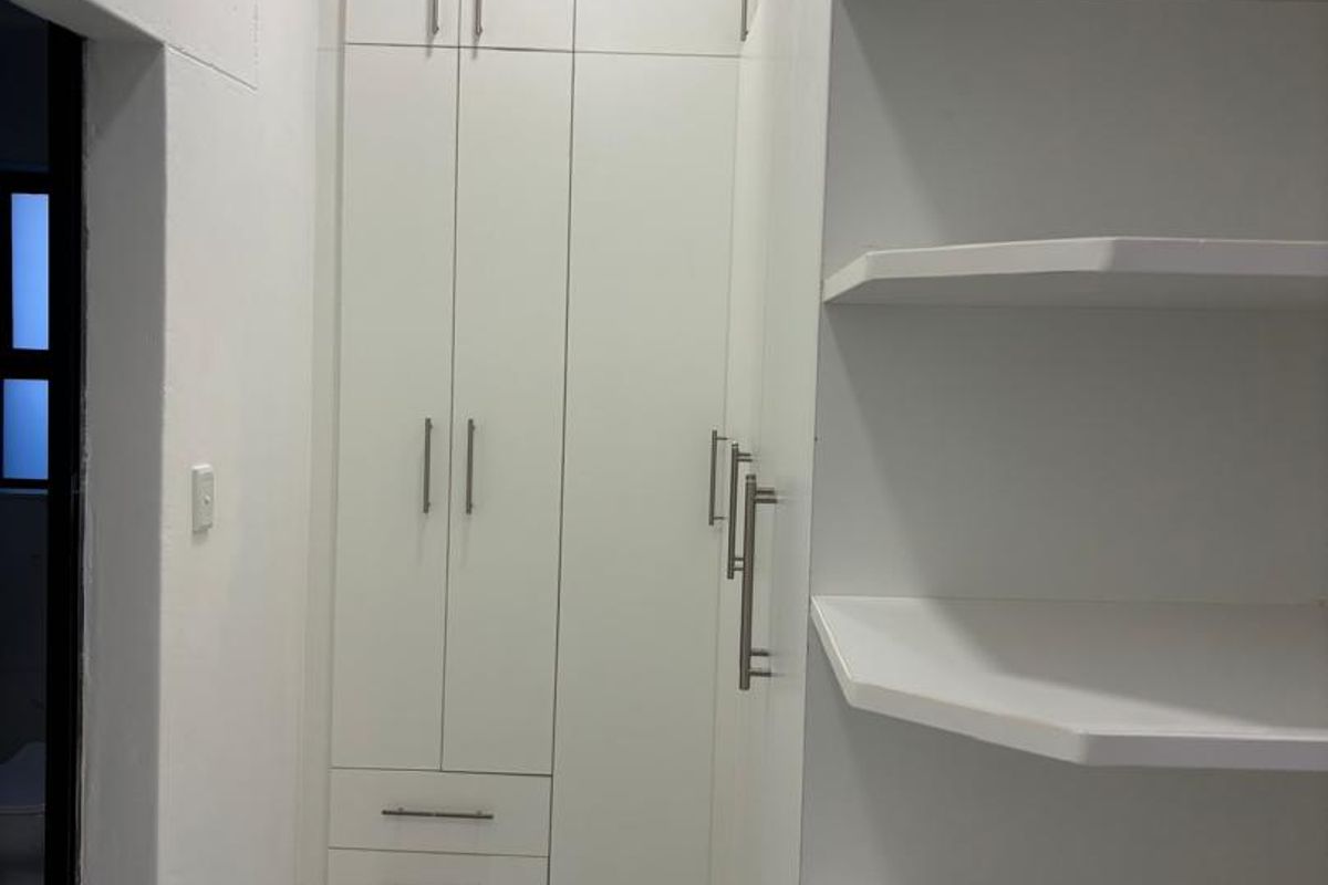 A clean, modern dressing area or bedroom space featuring white built-in cupboards, open shelving, and polished marble-look tiled flooring.