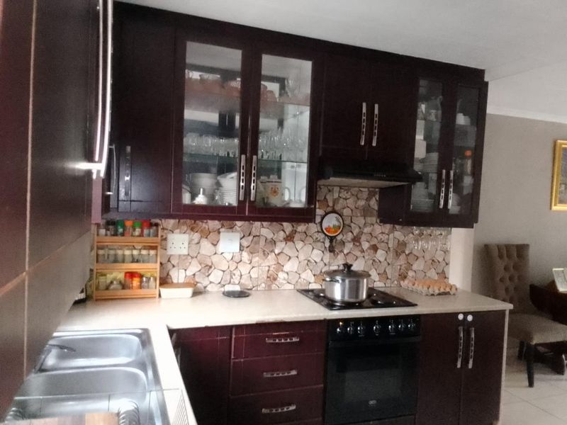 A functional kitchen featuring dark wood cabinetry, a stone-look mosaic backsplash, built-in oven with gas hob, and a double bowl stainless steel sink.