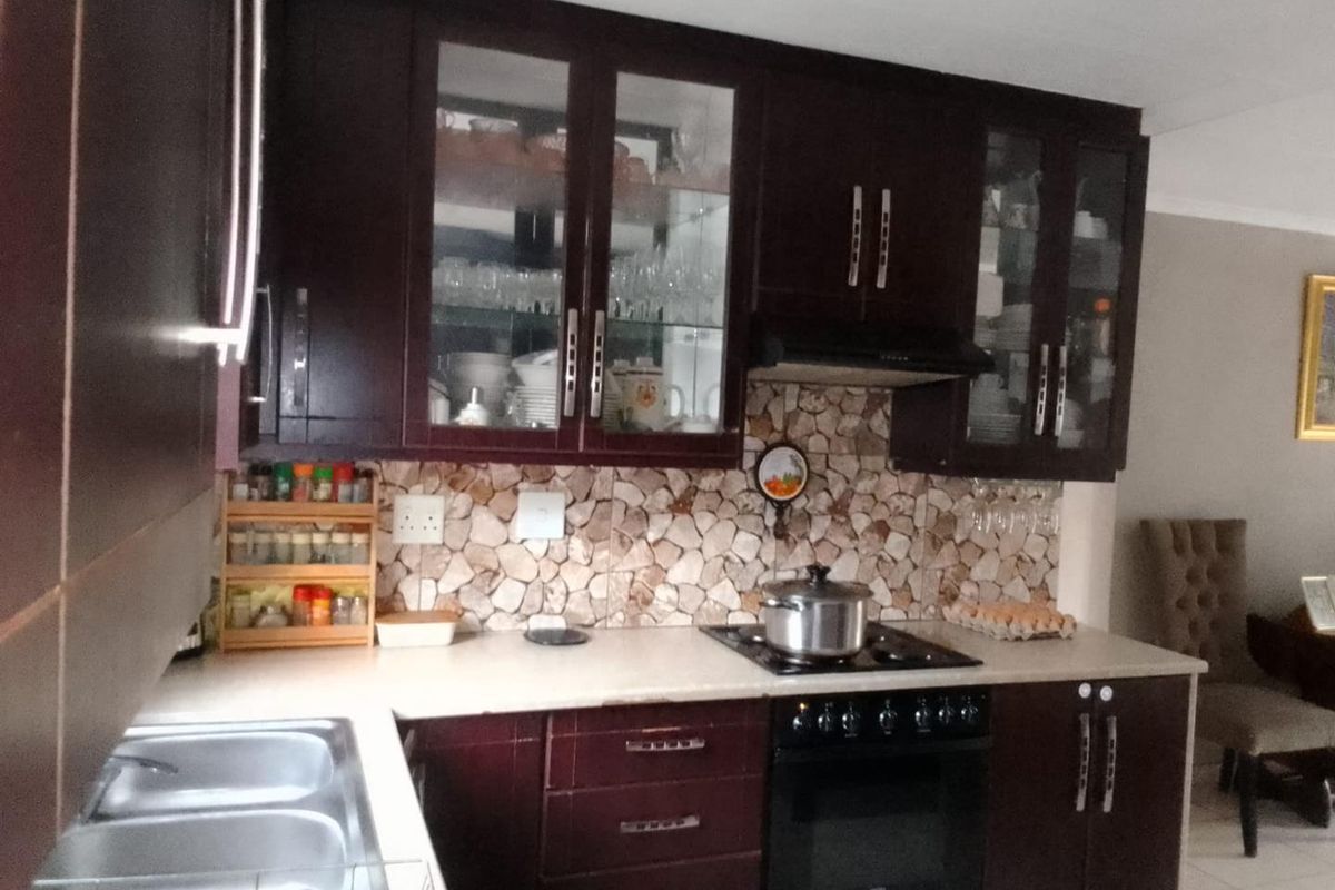A functional kitchen featuring dark wood cabinetry, a stone-look mosaic backsplash, built-in oven with gas hob, and a double bowl stainless steel sink.