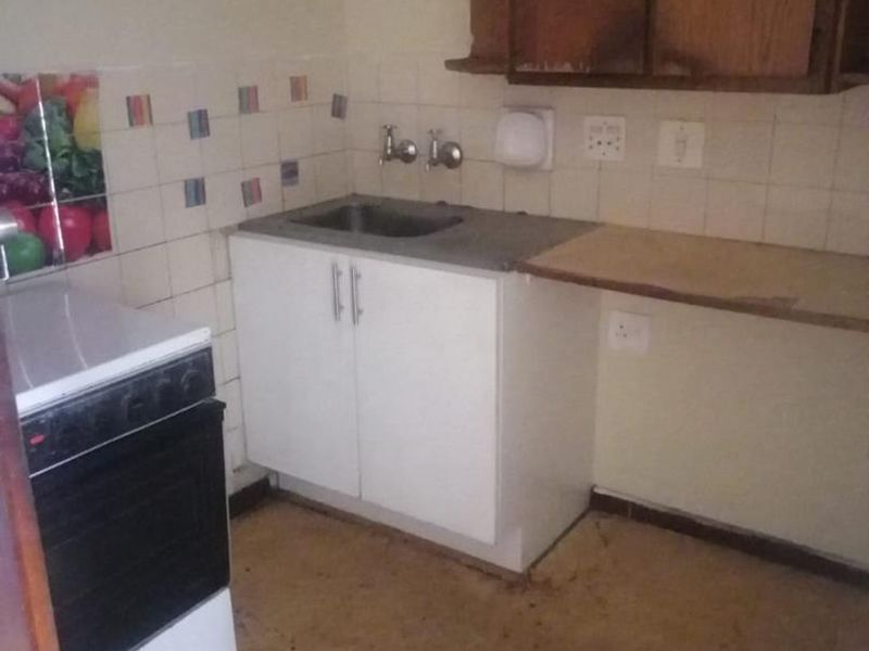 A dated kitchen area featuring basic cabinetry, a stainless steel sink, and a freestanding stove, requiring modernization and cosmetic updates.