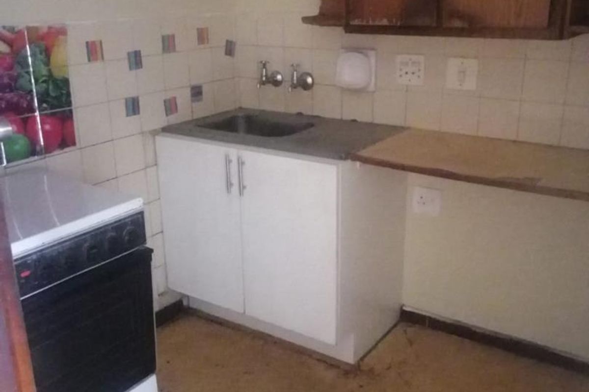 A dated kitchen area featuring basic cabinetry, a stainless steel sink, and a freestanding stove, requiring modernization and cosmetic updates.