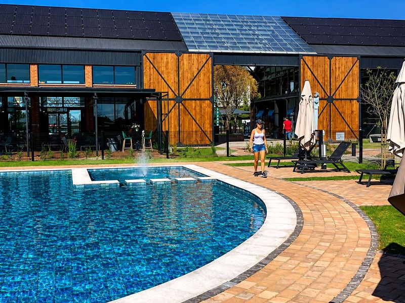 A well-maintained outdoor swimming pool area featuring a water fountain, paved surround, and modern architectural building facade with solar panels.