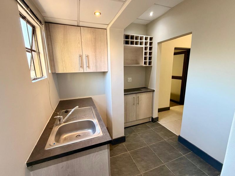 A clean and functional scullery featuring built-in cabinetry, laminate countertops, a stainless steel sink, and dedicated wine storage.