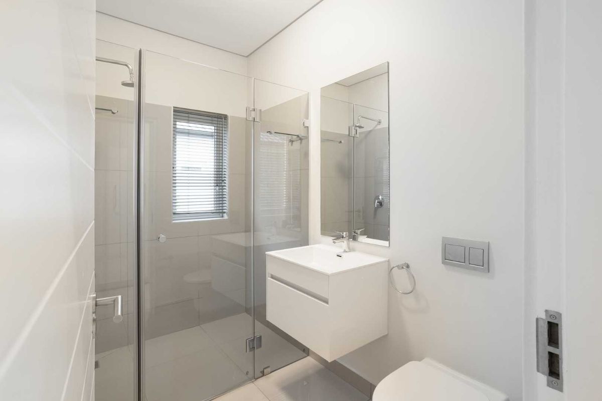 Modern, minimalist bathroom featuring a wall-mounted vanity, glass-enclosed shower, and concealed cistern toilet with neutral tiling.