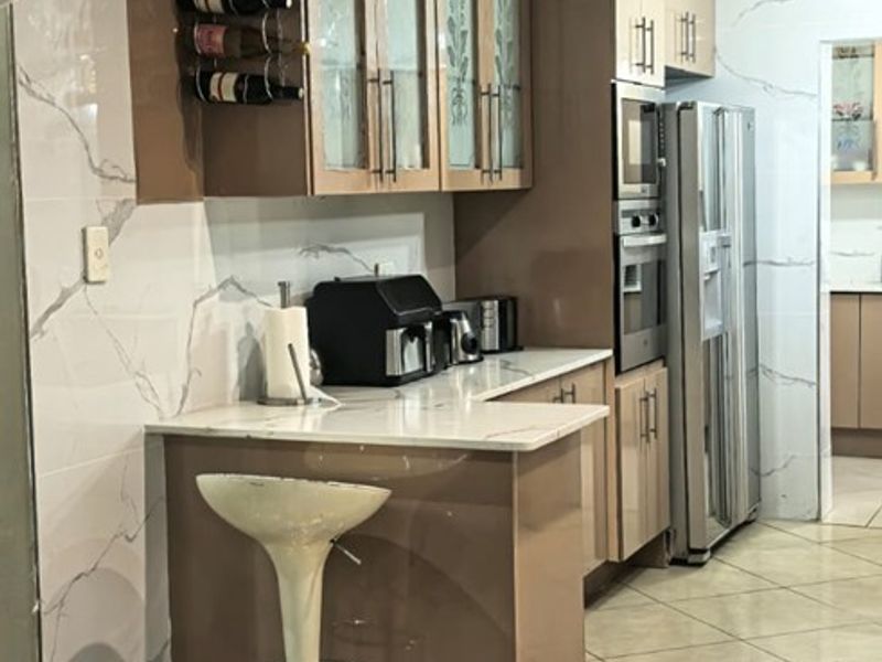 Modern kitchen featuring high-gloss cabinetry, stone countertops, integrated appliances, and elegant marble-look wall tiling with polished ceramic floor tiles.