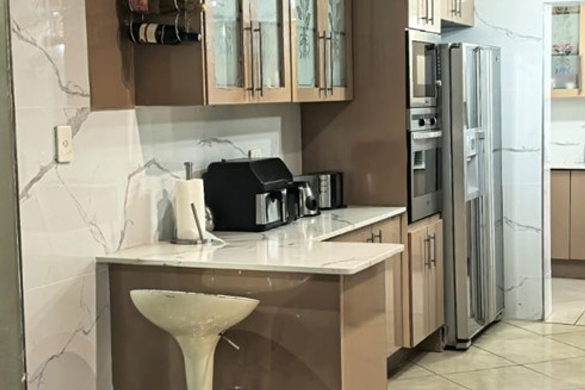 Modern kitchen featuring high-gloss cabinetry, stone countertops, integrated appliances, and elegant marble-look wall tiling with polished ceramic floor tiles.