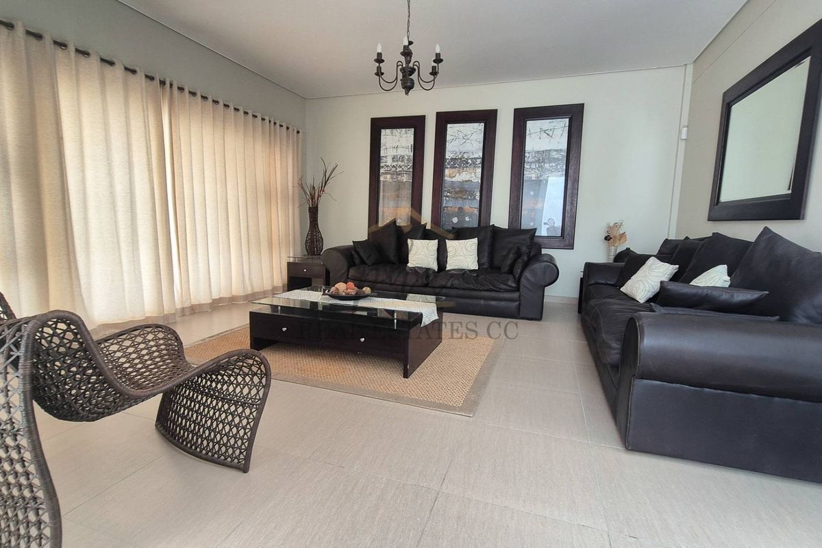 Spacious living room featuring neutral floor tiles, large sliding doors with curtains, and decorative wall panels.