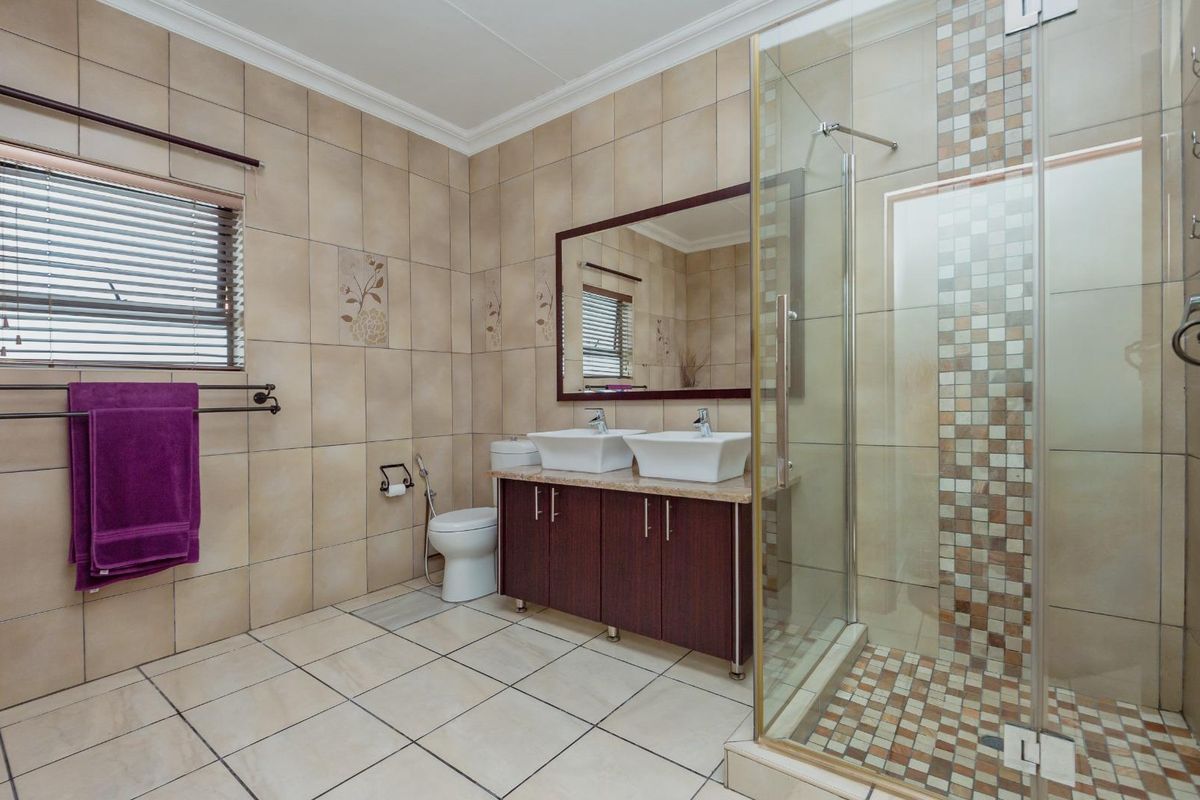 A spacious bathroom featuring a double vanity with vessel sinks, a glass-enclosed shower, and neutral floor-to-ceiling tiling.