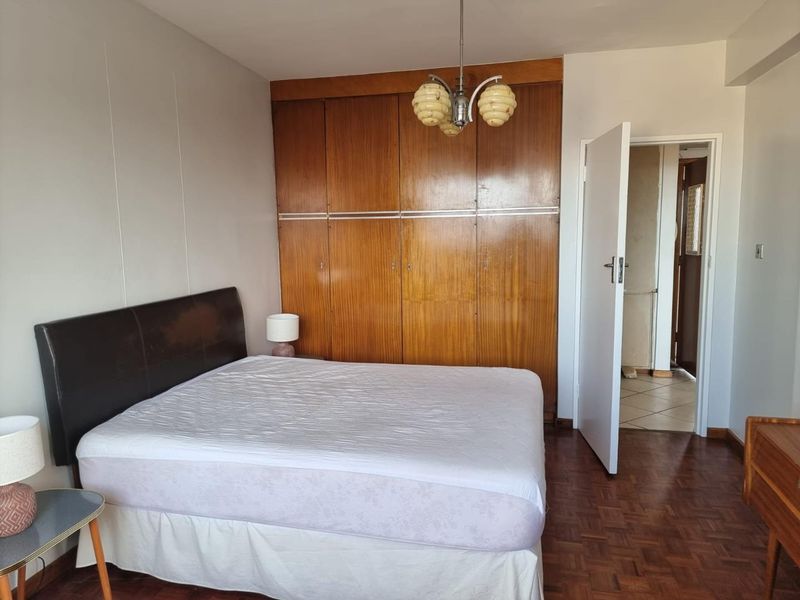 A bedroom featuring classic parquet flooring and a large built-in wooden wardrobe, offering a functional space with potential for modern updates.