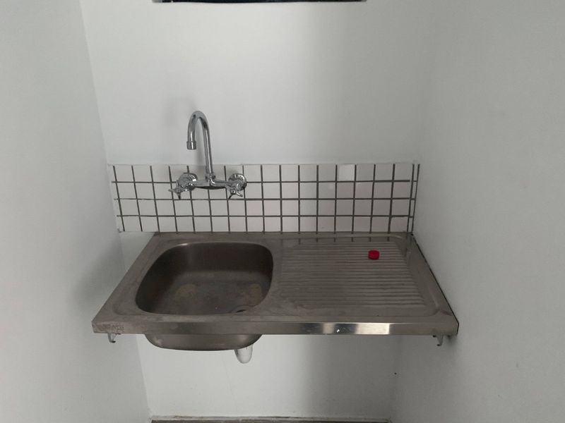 A basic utility sink area featuring a stainless steel basin, wall-mounted faucet, and a simple tiled splashback.