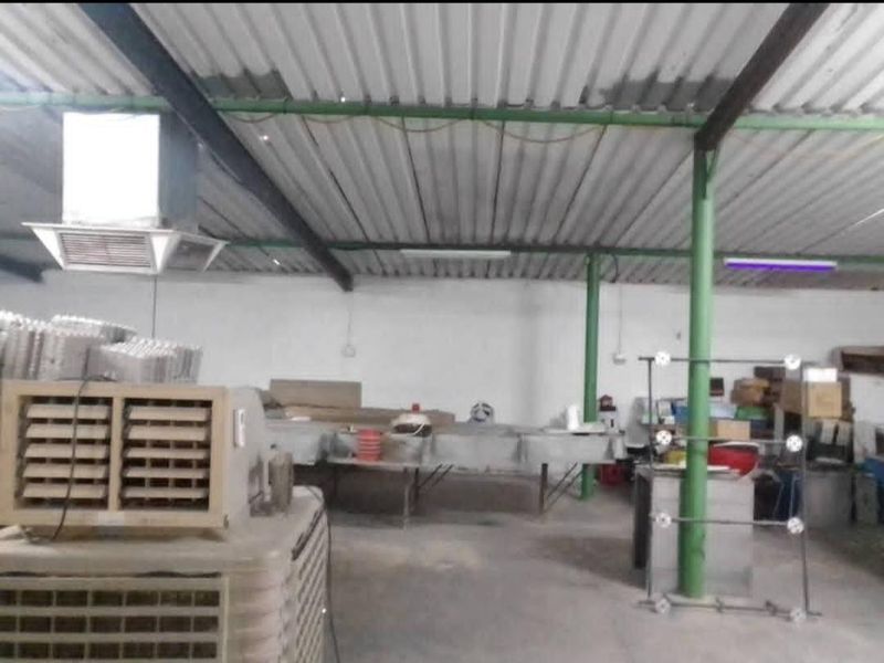 A large utility or storage space featuring a corrugated metal roof, steel support columns, and industrial lighting, suitable for workshop or agricultural use.