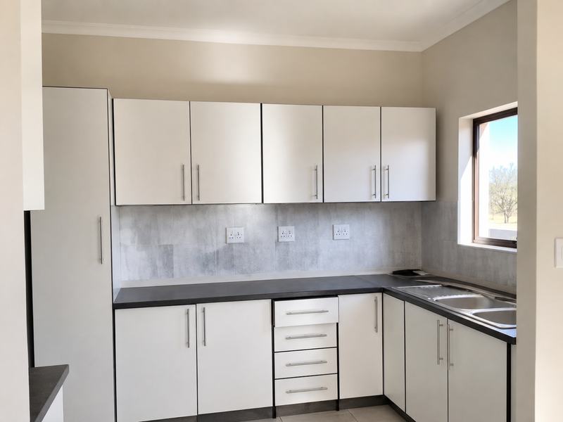 A clean, modern kitchen featuring white cabinetry, dark laminate countertops, a stainless steel sink, and a neutral tiled backsplash.