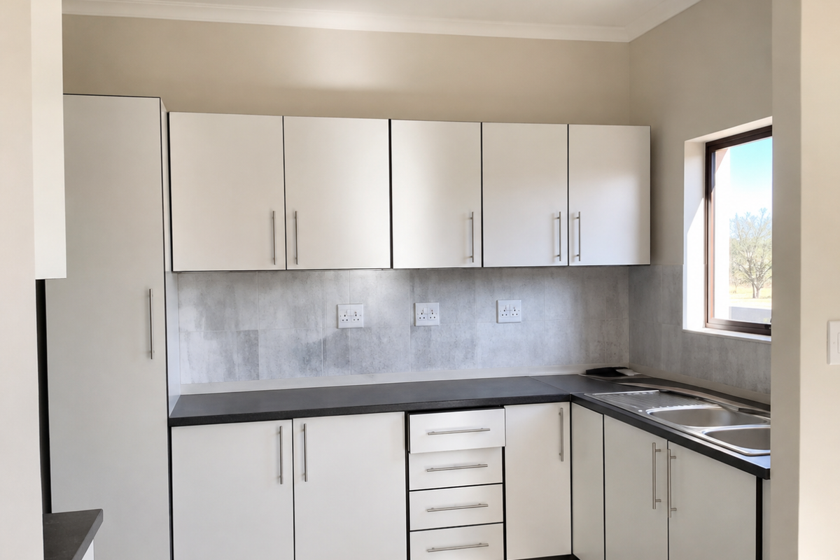 A clean, modern kitchen featuring white cabinetry, dark laminate countertops, a stainless steel sink, and a neutral tiled backsplash.