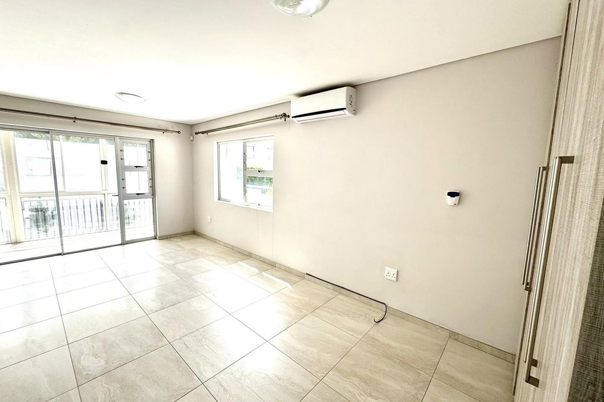 Bright and spacious living area featuring large format floor tiles, a wall-mounted air conditioning unit, and sliding glass doors leading to a balcony.