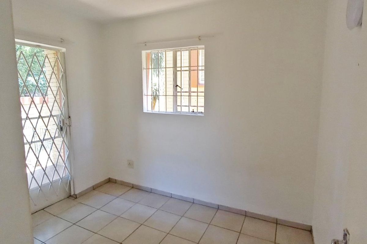 A simple, empty bedroom featuring tiled flooring, a security gate on the door, and a window with security bars.