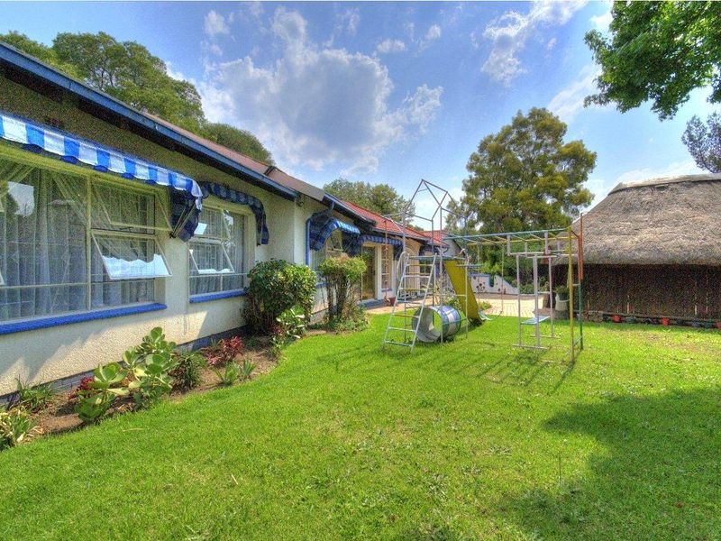 Rear garden view featuring a well-maintained lawn, a detached thatched structure, and the rear facade of the house with blue striped window awnings.