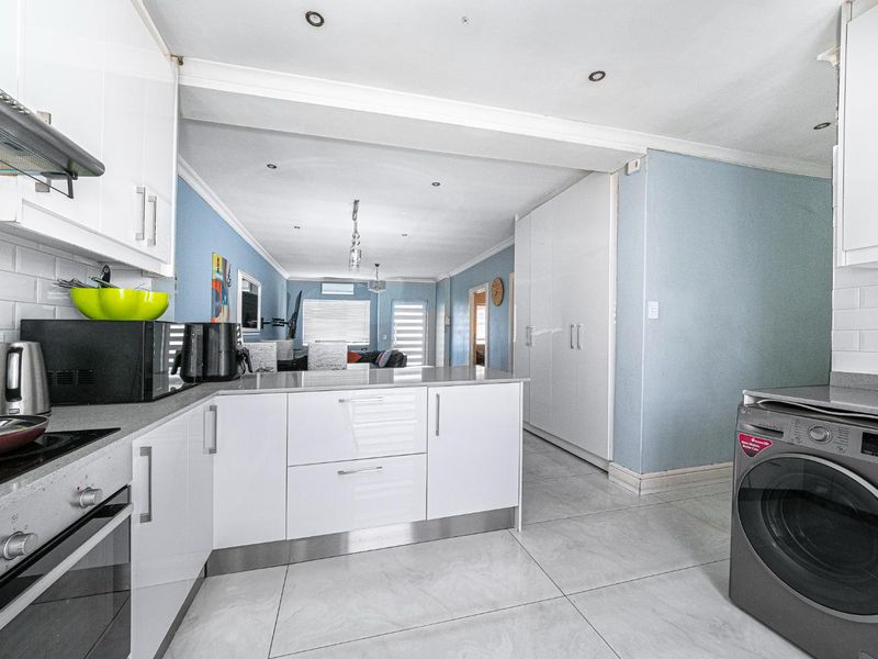 Open-plan kitchen featuring modern white cabinetry, stone countertops, and integrated appliances, flowing seamlessly into the adjacent living area with tiled flooring throughout.
