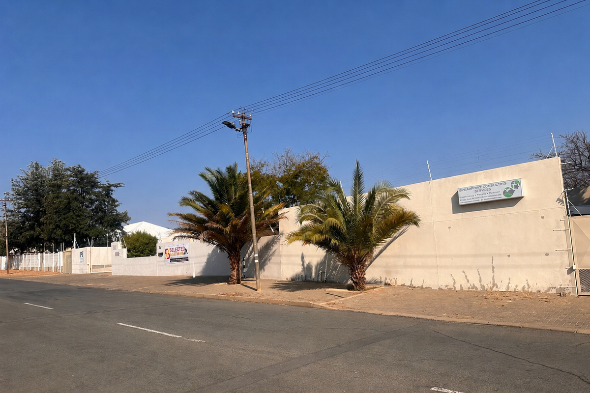 Street view of the property featuring a perimeter wall with electric fencing, paved sidewalk, and signage for Spearpoint Consulting Services.