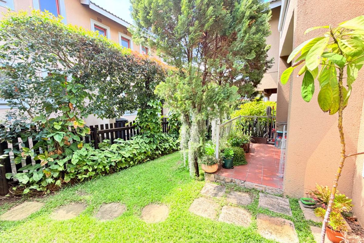 A private rear garden featuring a tiled patio area, stone stepping stones, and established greenery with a timber boundary fence.