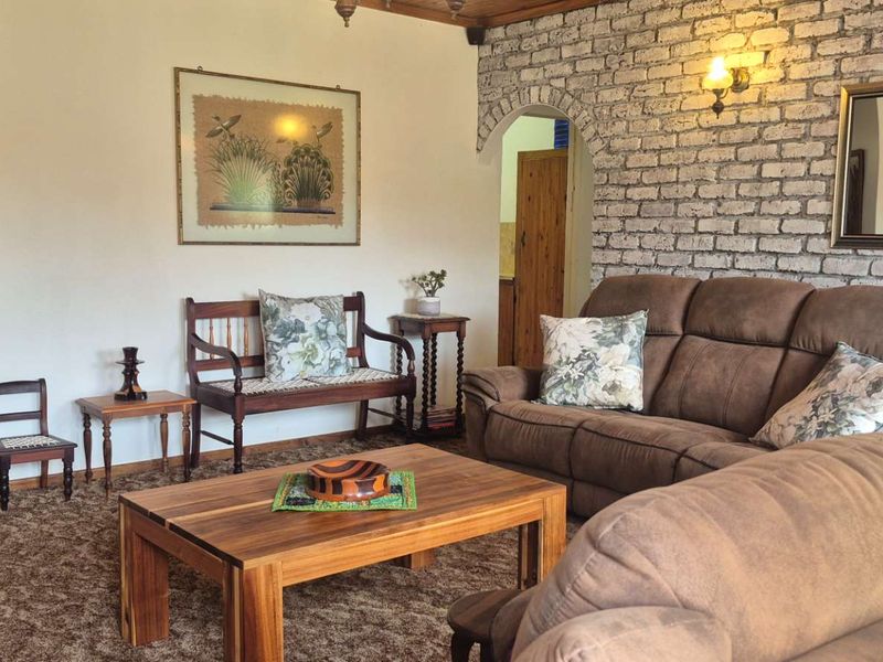 A living room featuring a rustic exposed brick wall, timber ceiling accents, and an arched doorway leading to adjacent living spaces.