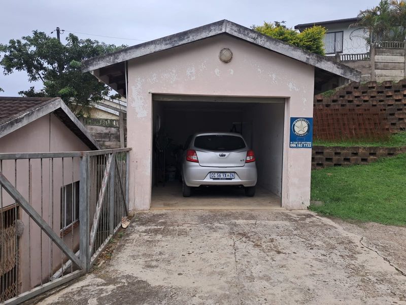 A detached single garage with a concrete driveway and visible exterior wear, featuring a pitched roof and an integrated security sign.