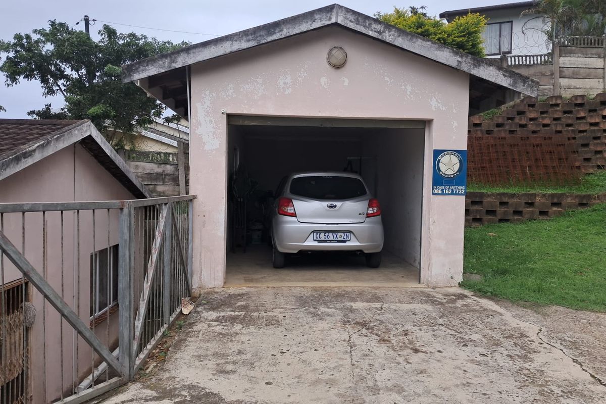 A detached single garage with a concrete driveway and visible exterior wear, featuring a pitched roof and an integrated security sign.