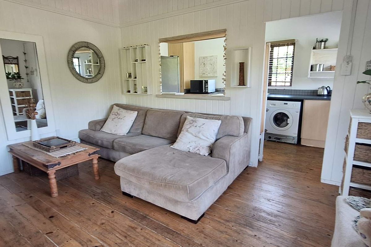 Cozy living room featuring timber flooring and wall paneling, with a convenient pass-through window connecting to the adjacent kitchen and laundry area.