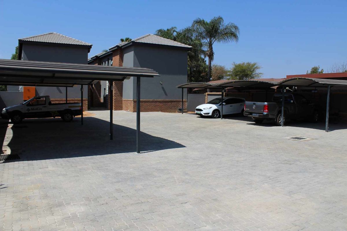 An outdoor parking area featuring multiple covered carports and a paved driveway within an apartment complex.