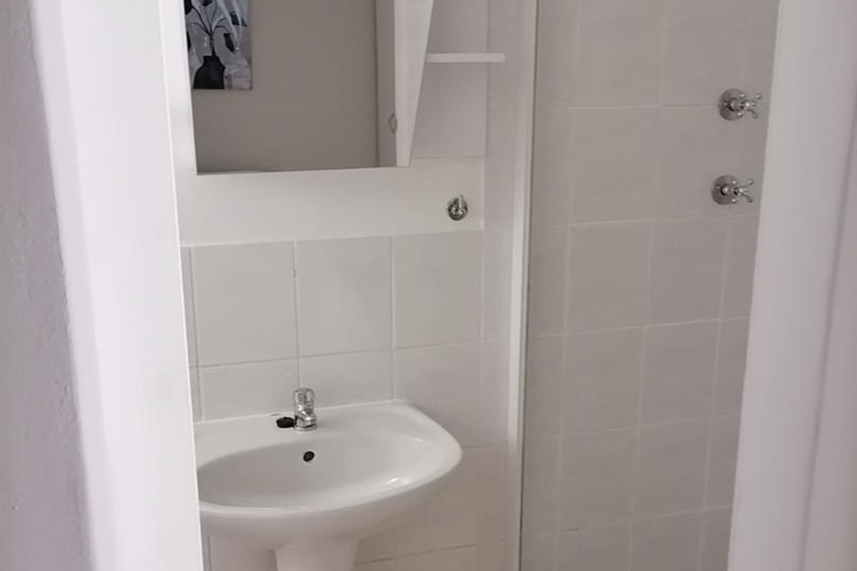 A functional bathroom featuring a pedestal basin, wall-mounted mirror, and a tiled shower enclosure.