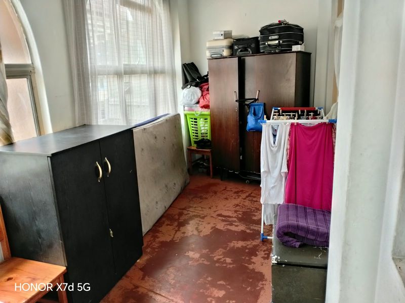 A bedroom space featuring an arched window and worn concrete flooring, currently used for storage.