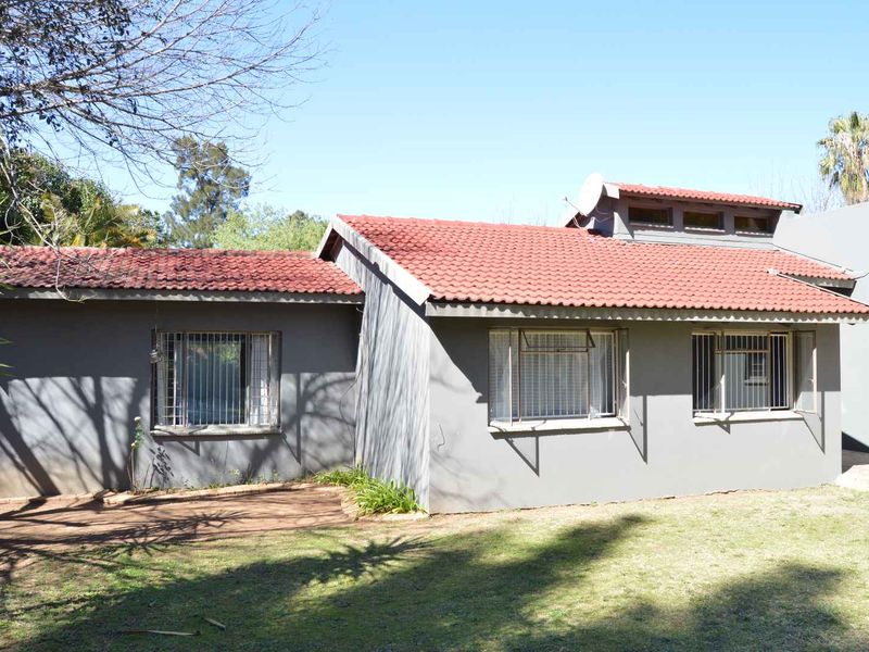 Rear view of a single-story house featuring a terracotta tiled roof, grey painted exterior walls, and security bars on the windows.