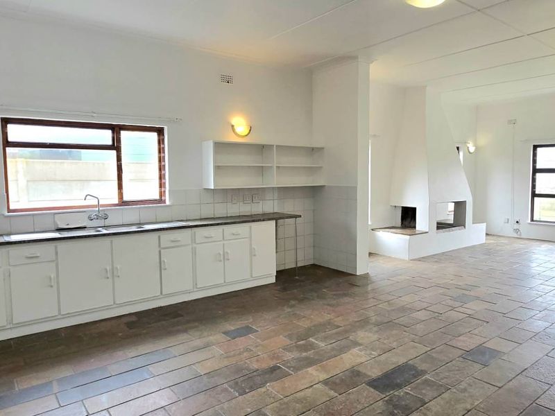 Spacious open-plan living area featuring a functional kitchen with built-in cabinetry, tiled flooring, and a prominent built-in fireplace.