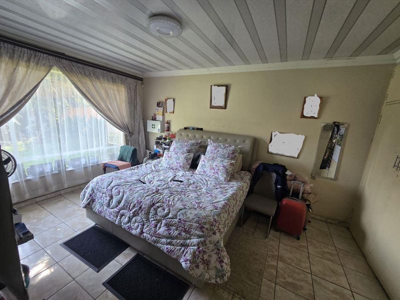 A bedroom featuring tiled flooring and a large window, providing natural light. The space would benefit from cosmetic updates to the walls and ceiling.