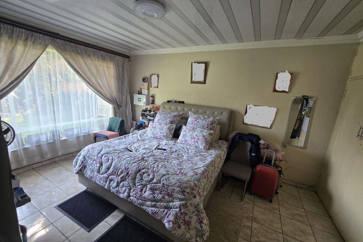 A bedroom featuring tiled flooring and a large window, providing natural light. The space would benefit from cosmetic updates to the walls and ceiling.