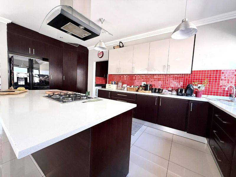 Modern kitchen featuring a central island with gas cooktop, dark wood cabinetry, contrasting white upper cabinets, and a vibrant red tiled backsplash.