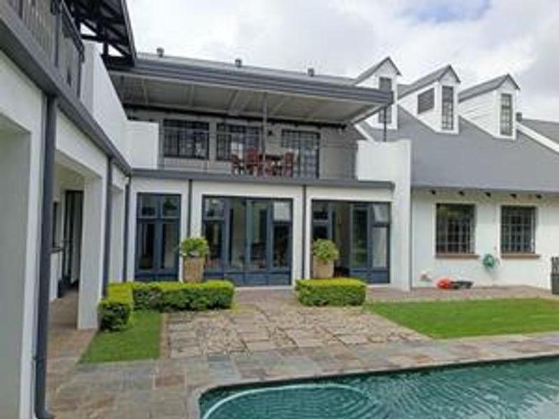 Rear view of the property featuring a swimming pool, stone patio, upper-level balcony, and well-maintained garden with modern architectural detailing.