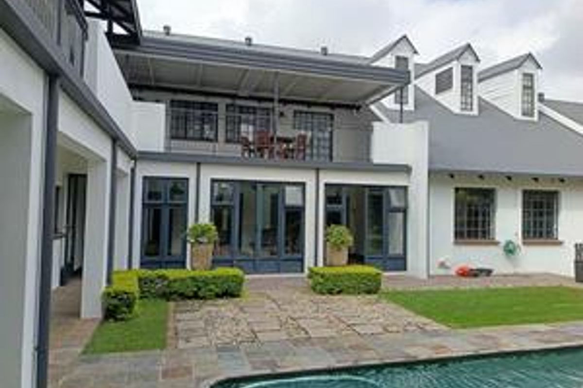 Rear view of the property featuring a swimming pool, stone patio, upper-level balcony, and well-maintained garden with modern architectural detailing.