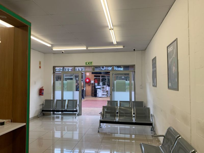 A functional retail entrance area featuring tiled flooring, drop ceilings with fluorescent lighting, and glass doors leading to an exterior walkway.