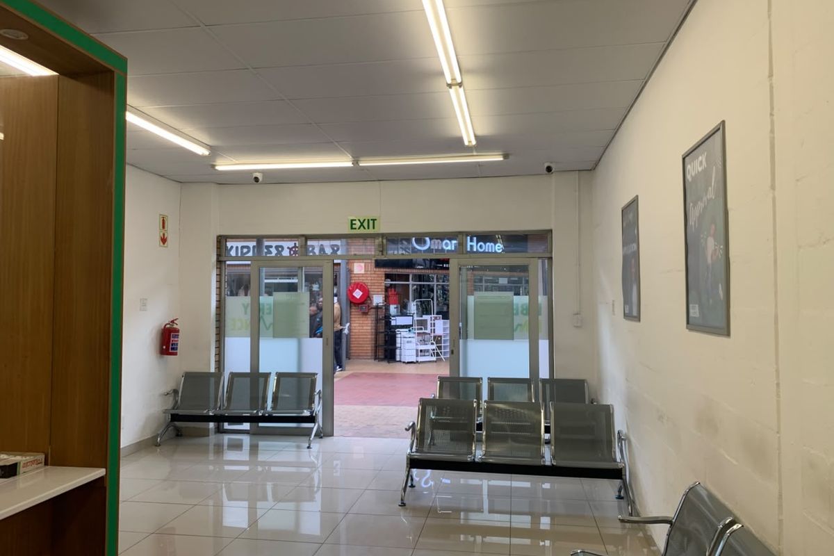 A functional retail entrance area featuring tiled flooring, drop ceilings with fluorescent lighting, and glass doors leading to an exterior walkway.