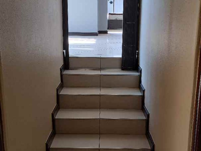 A narrow tiled hallway featuring a small staircase leading to an adjacent living area, showing signs of wear on the flooring and walls.